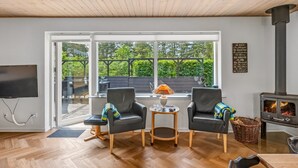 Un salon chaleureux avec une cheminée, deux fauteuils en cuir, une petite table avec une lampe et un téléviseur.