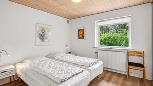 Une chambre avec deux lits, une fenêtre donnant sur un espace verdoyant, un plafond en bois et un radiateur.