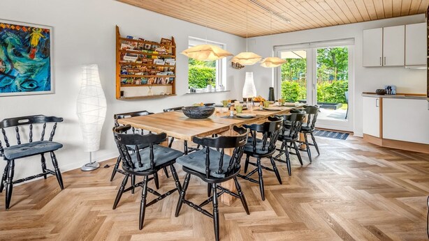 Un coin repas avec une table et des chaises en bois, une bibliothèque et une grande fenêtre donnant sur un paysage verdoyant.