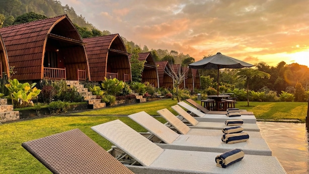 Una hilera de cabañas de madera con balcones, un área de lounge junto a la piscina con tumbonas y una mesa de comedor.