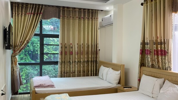 Ein Hotelzimmer mit zwei Betten, einem Deckenventilator, einer Klimaanlage und einem Fenster mit Vorhängen.