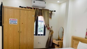 Ein Hotelzimmer mit Holzschrank, Bett mit weißer Bettdecke, Nachttisch mit Spiegel und einem Fenster mit Vorhängen.