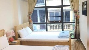 Ein Hotelzimmer mit zwei Betten, einer Kandelaber, einem Balkon mit Geländer und einem Fenster mit Vorhängen.