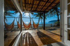 A wooden deck with hammocks, a glass door, and a view of the ocean and palm trees.
