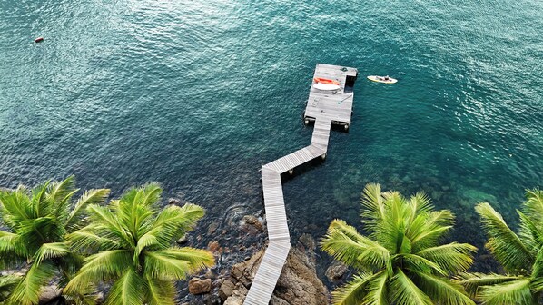 A wooden pier extending into turquoise water, surrounded by palm trees.