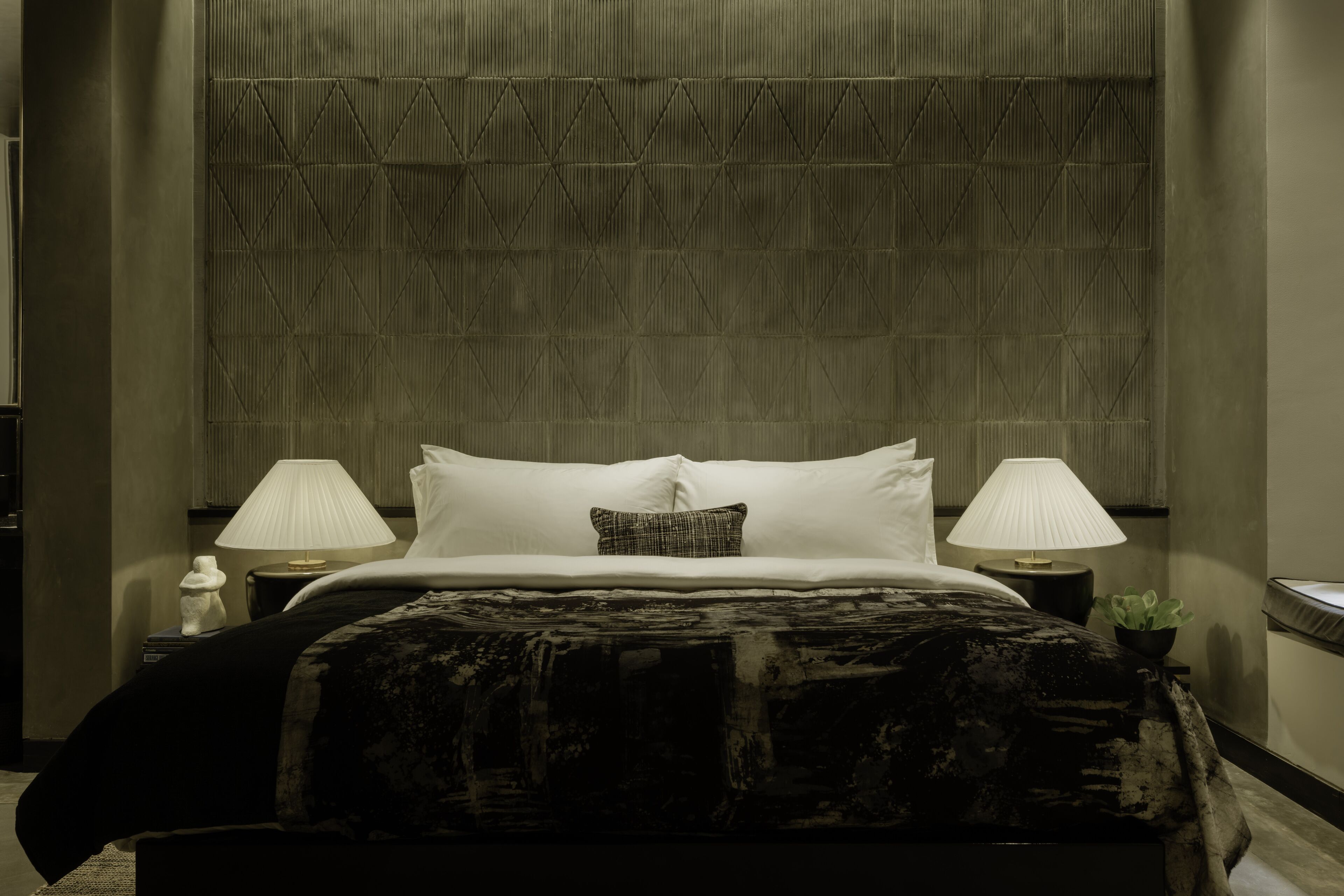 Una cama bien hecha con sábanas blancas y una sola almohada decorativa, flanqueada por dos lámparas de noche en mesitas a juego.