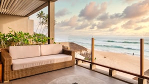 A balcony with a wicker sofa and a round table, overlooking a beach with palm trees and the ocean. - The Six Weligama (Ahangama)