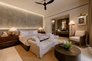 A modern hotel room with a large bed, a sofa, a round coffee table, a chair, and a ceiling fan. - The Six Weligama (Ahangama)