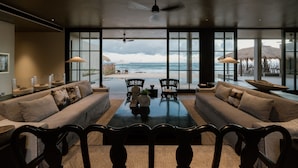 A spacious living room with a large window overlooking a beach, furnished with sofas and a coffee table. - The Six Weligama (Ahangama)