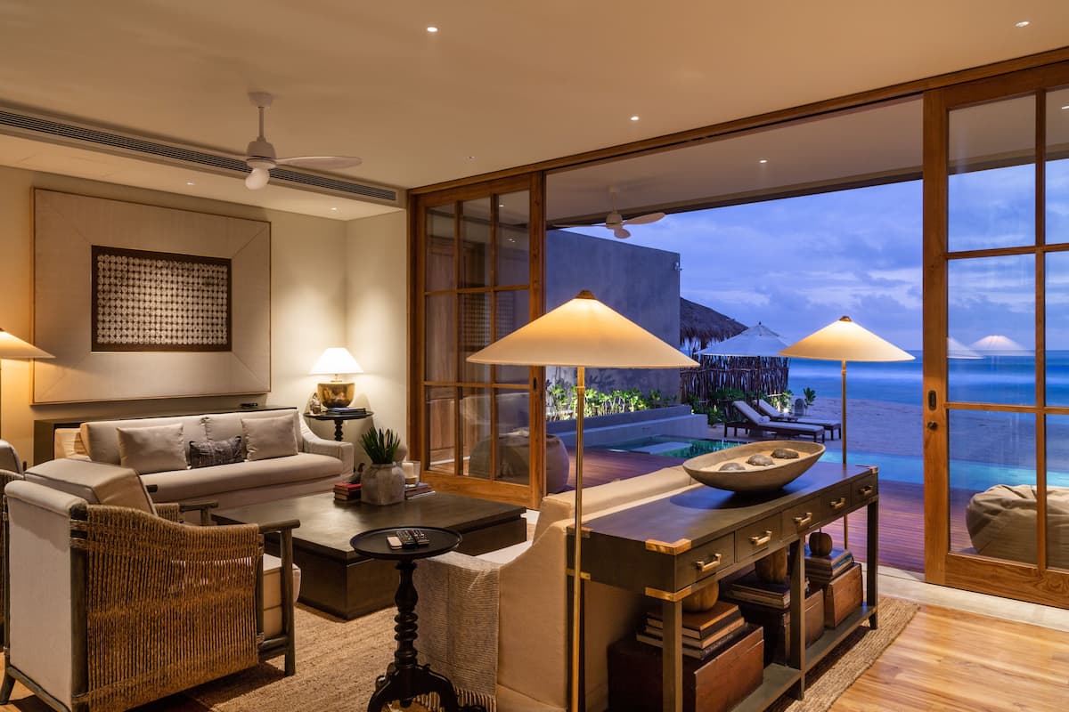 A modern living room with a large window overlooking a beach, a sofa, a coffee table, and a dining area with a view.