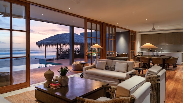 A spacious living area with a large window overlooking the beach, a cozy seating arrangement, and a modern kitchen in the background. - The Six Weligama (Ahangama)
