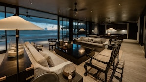 A modern living room with a large window overlooking a beach, furnished with sofas, a coffee table, and lamps. - The Six Weligama (Ahangama)