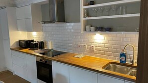 A compact kitchen with white cabinets, a wooden countertop, a built-in oven, and a stainless steel sink. - Stunning apartment by The Leas, West End (Folkestone)
