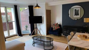 A modern living room with a glass coffee table, a TV on a tripod, a sofa, a dining table with chairs, and a fireplace. - Stunning apartment by The Leas, West End (Folkestone)