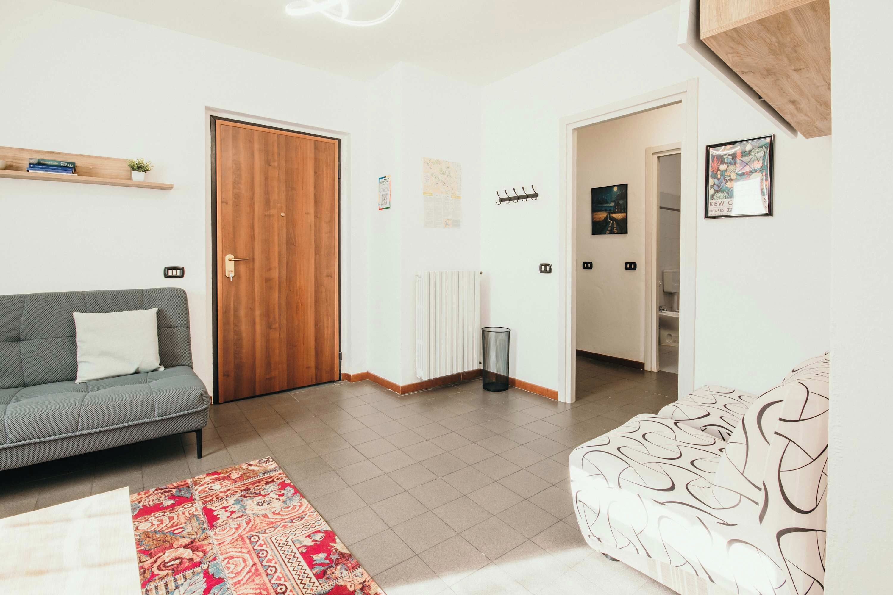 A living room with a grey sofa, a patterned sofa, a wooden door, and a radiator.