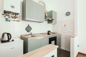 Una cocina compacta con estufa integrada, un lavamanos y una tetera sobre la encimera.