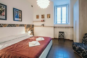 Ein Schlafzimmer mit Bett, Fenster, Stuhl und Wandbildern.