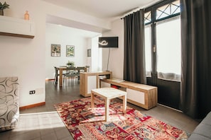 Una sala de estar moderna con un sofá, una mesa de centro, un televisor, un comedor con sillas y una mesa, y un gran ventanal con cortinas.