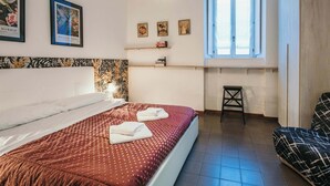Ein Schlafzimmer mit Bett, Fenster, Stuhl und Wandbildern.
