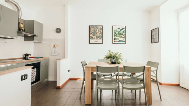 Eine moderne Küche mit Essbereich, ausgestattet mit einem Holztisch, Stühlen, einem kleinen Topf mit Pflanze und zwei gerahmten Bildern an der Wand.