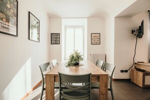 Een eetgedeelte met een houten tafel, zes stoelen, een bloempot en kunstwerken in lijsten aan de muren.