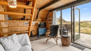 A cozy cabin interior with a wooden ceiling, a sofa, a television, and a large sliding glass door leading to an outdoor deck. - "Fausta" - 150m from the sea by Interhome (Ringkøbing)
