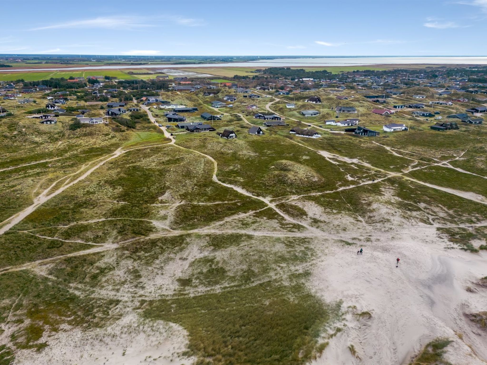 Vista aérea de un pueblo costero con casas dispersas sobre terreno arenoso, unidas por caminos sinuosos.