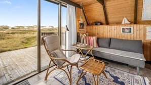 A cozy room with a wooden ceiling, a sofa, a chair, a small table, and a view of the landscape through large windows. - "Fausta" - 150m from the sea by Interhome (Ringkøbing)