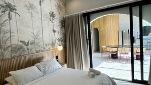 Hotelkamer met een groot bed, een muurschildering en een glazen schuifdeur naar een buitenruimte met tafels en stoelen.