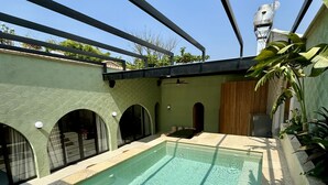 Zwembad met betegeld zonnedek, een pergola erboven en een waterpartij aan de rechterkant.