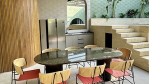 Een terras buiten met een ronde tafel en stoelen, een plafondventilator, en een keuken met een koelkast en fornuis.