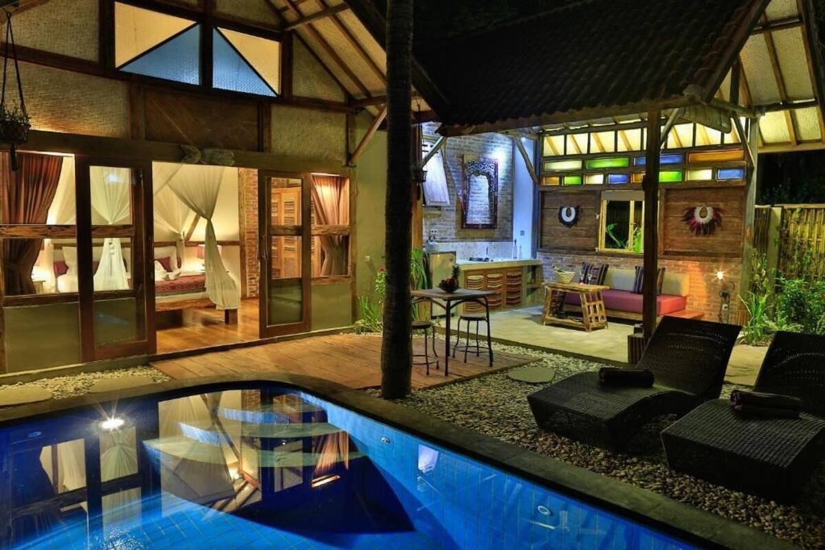 Un área junto a la piscina con vista despejada a un dormitorio con cama y cortinas, un comedor con mesa y sillas, y una pequeña cocina.