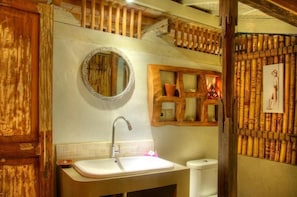 Une salle de bain au style rustique, avec un meuble-lavabo en bois, un miroir rond et une petite étagère ornée d’objets décoratifs.