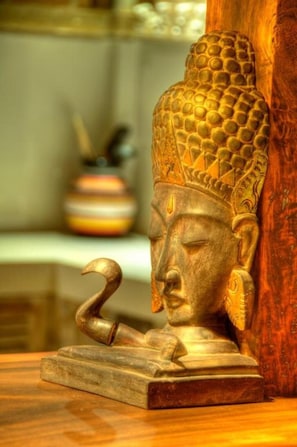 Une statue de Bouddha tenant un bâton recourbé, posée sur un socle en bois.