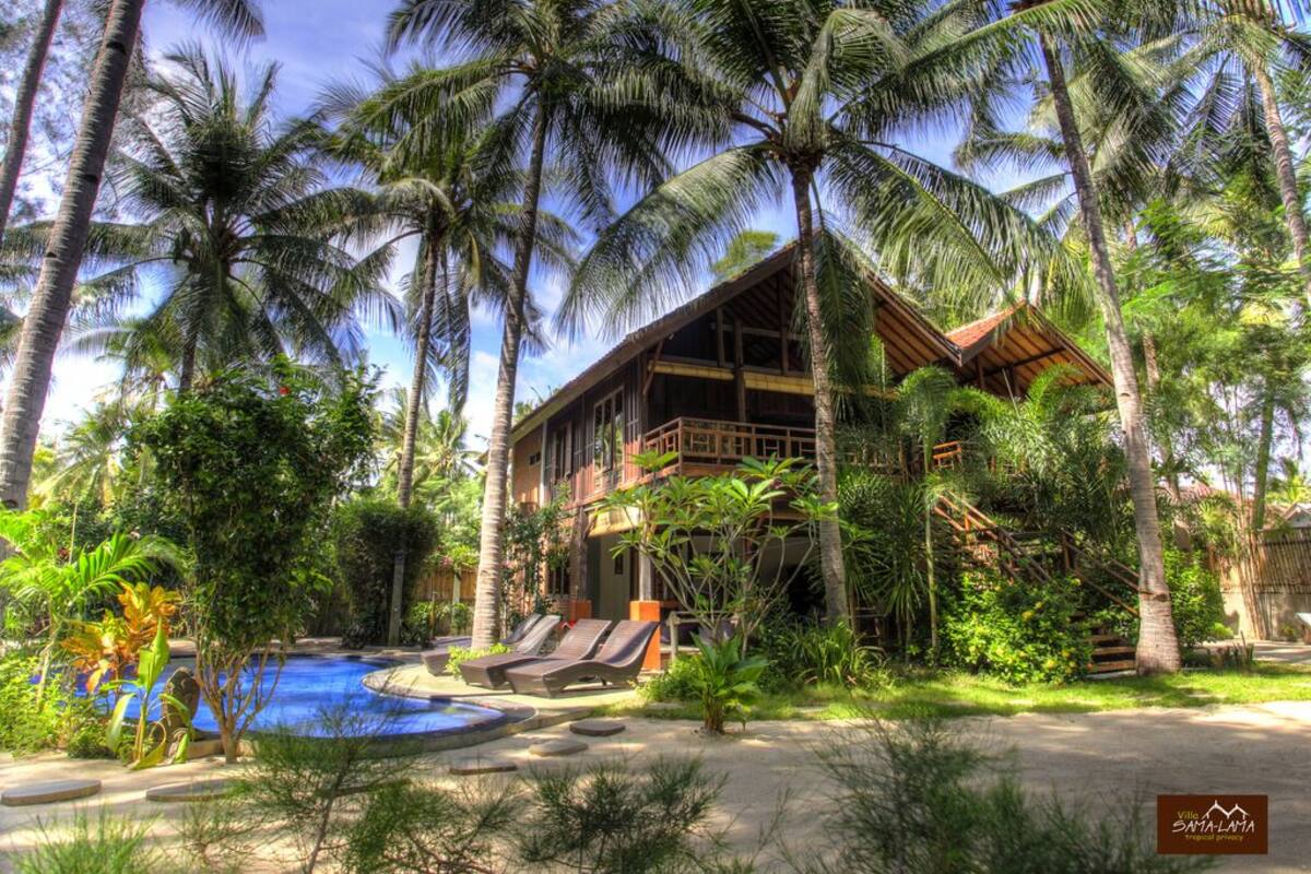 Un resort con piscina, palmeras y un edificio de madera con balcón.