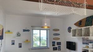 A cozy living room with a large window, a television, and various wall decorations. - Fonte da Telha Beach Hostel (Almada)