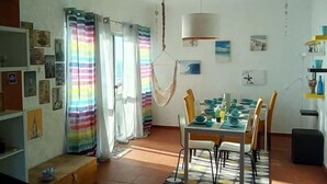 A dining area with a table set for four, surrounded by chairs, a hanging light fixture, and a patterned rug. - Fonte da Telha Beach Hostel (Almada)