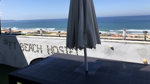 A patio with a table and an umbrella overlooking a beach. - Fonte da Telha Beach Hostel (Almada)