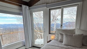 A bedroom with a large bed, a view of the outdoors, and a wooden ceiling.