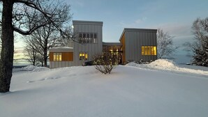 A modern house with a symmetrical design, large windows, and a snow-covered landscape.