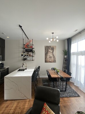 Uma cozinha moderna com uma ilha de mármore, área de jantar com mesa e cadeiras de madeira, e sala de estar com sofá e mesa de centro.
