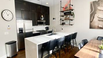 A modern kitchen with dark cabinets, a white island, and a dining area with a wooden table and chairs.