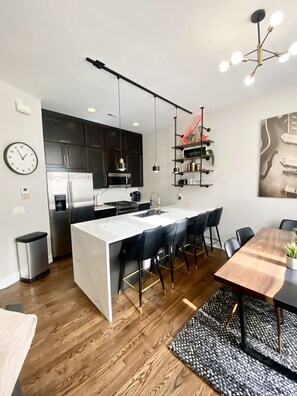 A modern kitchen with dark cabinets, a white island, and a dining area with a wooden table and chairs.