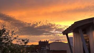A rooftop with a view of a sunset, featuring a metal railing and a small seating area.
