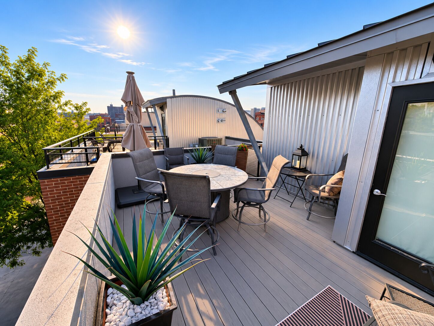A rooftop patio with a round table and chairs, surrounded by potted plants and a view of the city skyline.