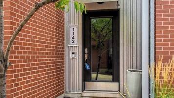 A brick building with a numbered door, a small pathway leading to the entrance, and a potted plant beside the door.