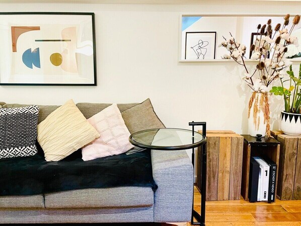 Ein Wohnzimmer mit grauem Sofa, schwarz-weißen Kissen, einem Glastisch und einem Bücherregal mit Büchern.