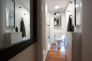 Ein schmaler Flur, der zu einem Badezimmer mit Toilette, Waschbecken und Spiegel führt.