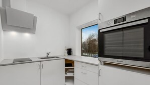 Eine moderne Küche mit weißen Schränken, einem Edelstahlbackofen und einem Fenster mit Blick nach draußen.
