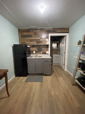 A kitchen with a black refrigerator, grey cabinets, a wooden floor, and a door leading to another room. - Simple luxury in a country setting  (Idaho Falls)
